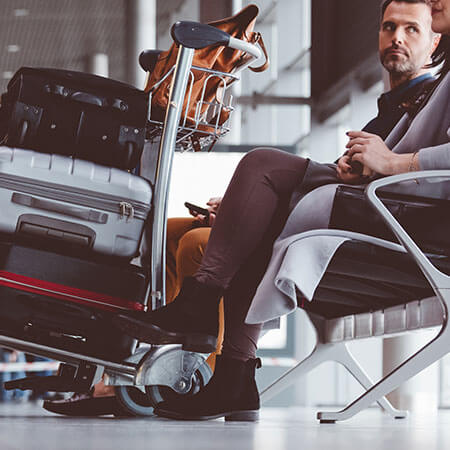 man moving to dublin sits on seat in airport with trolley full of suitcases