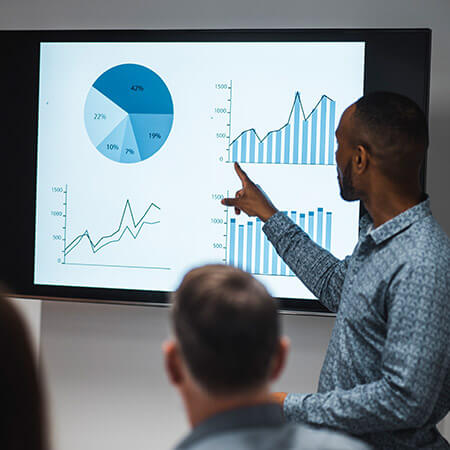 man pointing at presentation on screen which features bar charts and graphs about investment opportunities