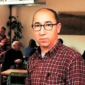 hassan lemtouni stand in blas café wearing a check shirt and black glasses