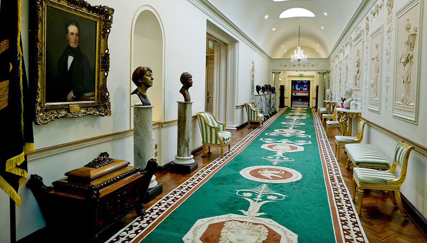 a highly decorated hallway lined with chairs, paintings, and busts