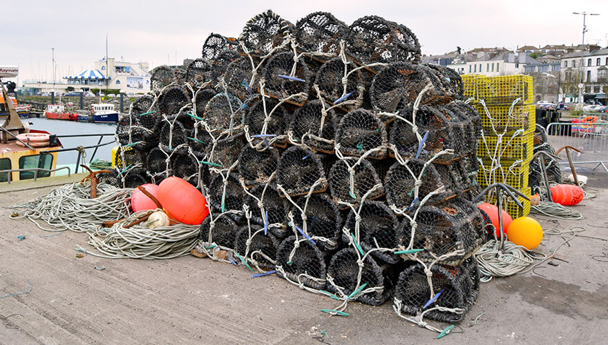 black netted lobster pots are piled high on a harbour