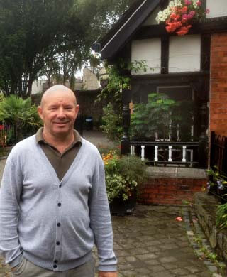 park keeper ed bowden smiles as he stands in front of the tudor lodge in a green cardigan and green polo shirt