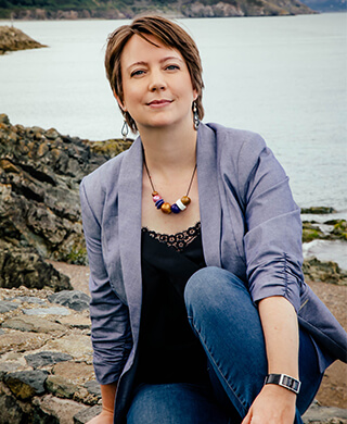 responsible innovation summit founder Szilvia Szabo sits on rocks along the coast