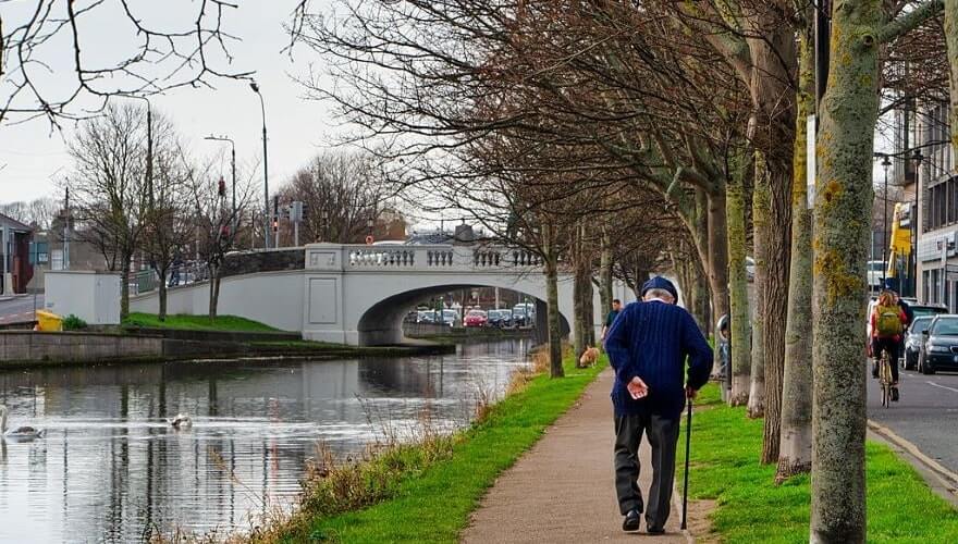 man with walking stick walking along the treelined canal