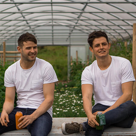theo and jack kirwan wear jeans and white t-shirts sitting side by side in a polytunnel