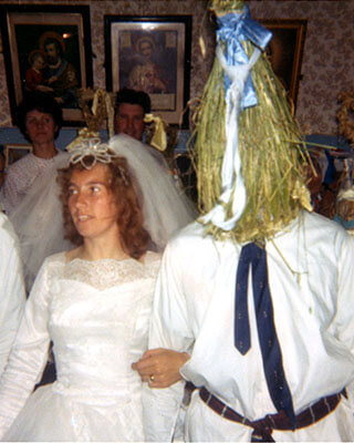 A photo of a bride wearing a wedding dress and linking arms with a 'Straw Boy' from the National Folklore Collection