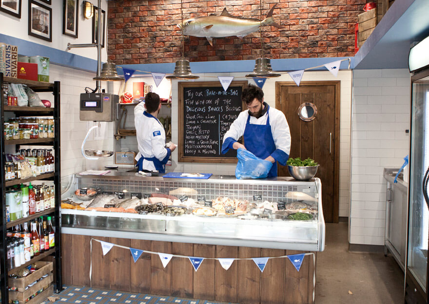 bunting hangs across a fish counter staffed by two men in aprons